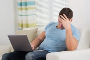 Man with headache sitting on sofa with a laptop