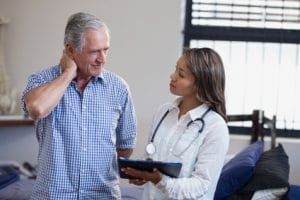 Senior man suffering from neck pain speaking with female doctor or therapist