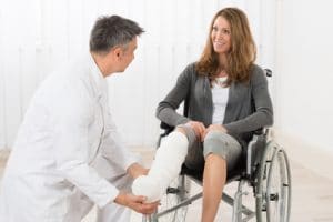 Doctor therapist examining leg of patient in cast and wheelchair