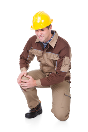 A man in a hardhat has sharp pain in his knee as he stands up while at work