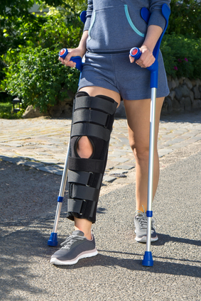 Woman wearing a knee brace after surgery and walking with crutches